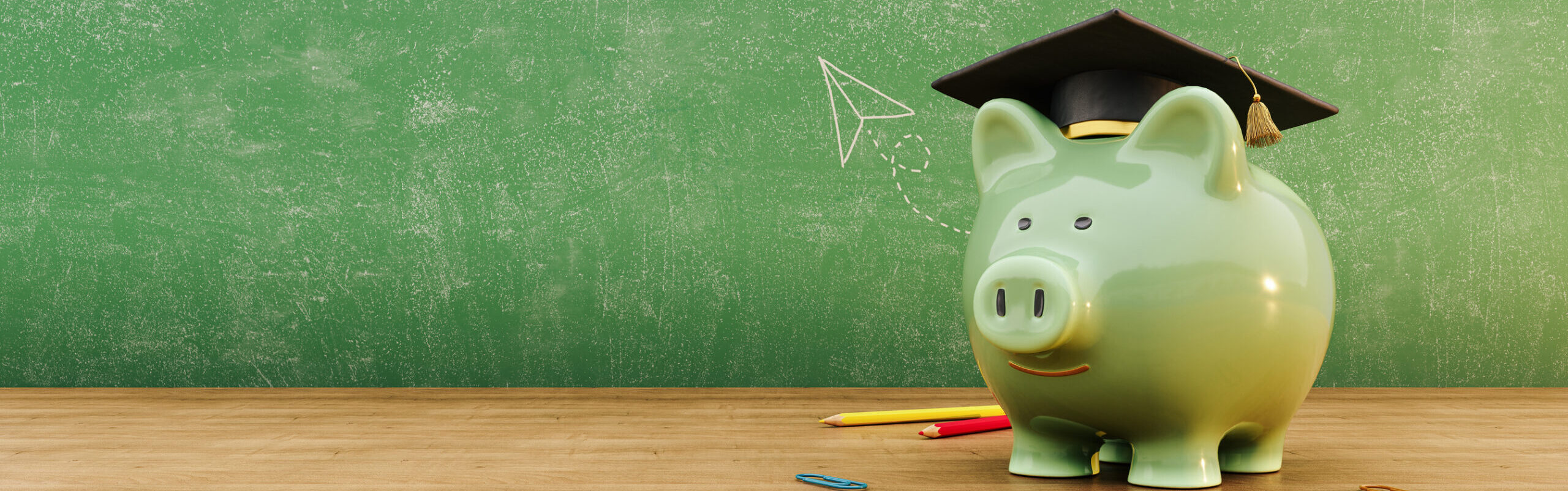 Green piggy bank wearing graduation hat in front of green chalkboard with copy space. Scholarship savings concept background.